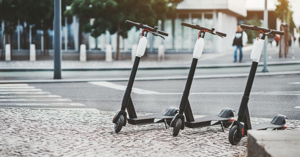 Photo of three electric scooters parked on a curb next to an empty intersection.