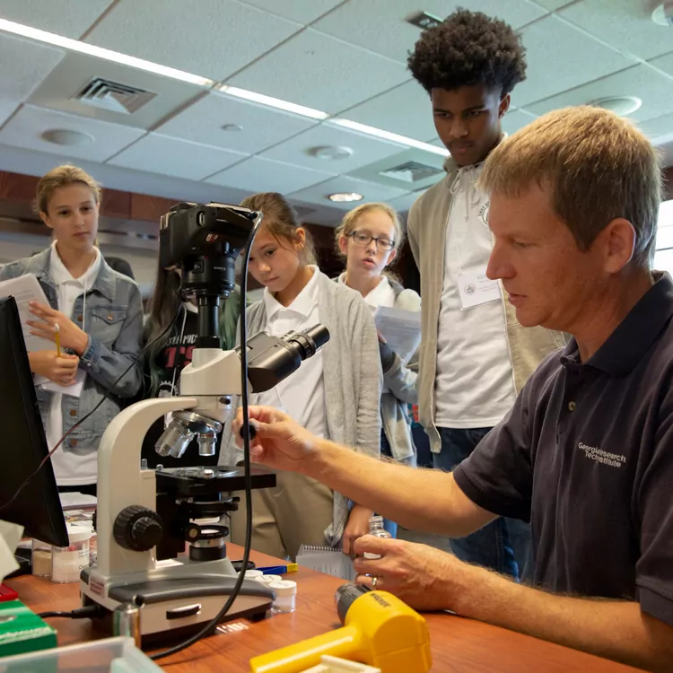 Science teacher showing children a microscope.