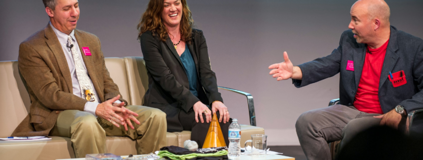 Three people laughing and having a conversation on stage