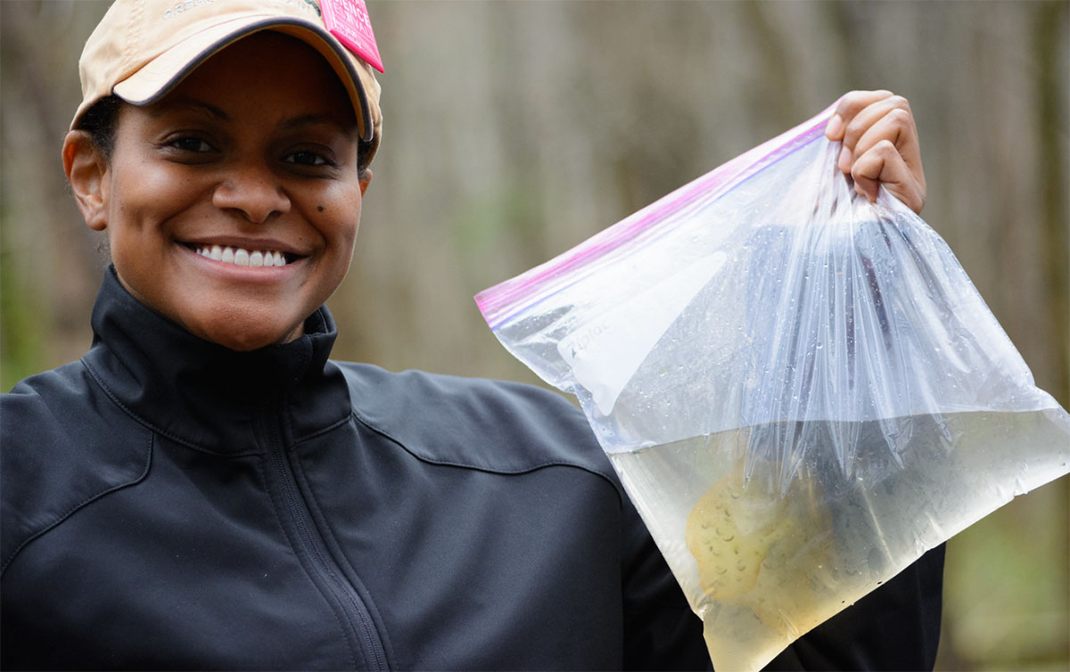 Crystal Mandica holding a plastic bag of natural water that has an amphibian inside.